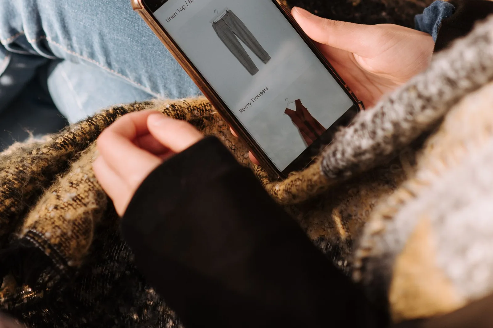 Een bezoeker bekijkt kleding op haar telefoon terwijl zij thuis zit.